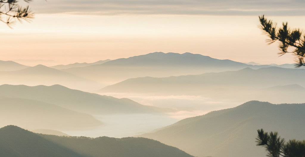 A serene photograph of a quiet mountain landscape at dawn, layered misty ridges receding into soft light, with a tranquil calm atmosphere. In the foreground, subtle silhouettes of pine branches. Muted natural palette of soft sage green, pale ivory mist, and gentle warm light. Evokes retreat, stillness, and returning to oneself. Photographic realism, spacious, refined, luxury travel aesthetic.